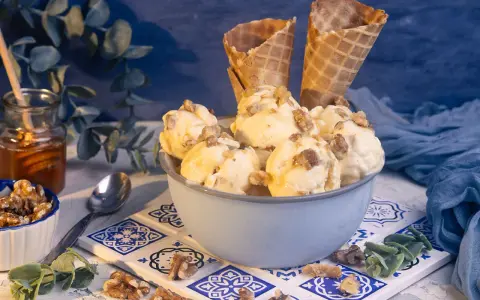 Schüssel mit Eiscreme, garniert mit Nüssen und Honig. Ein Glas Honig und Waffelhörnchen im Hintergrund. Ein süßer Genuss: Eis mit Honig statt Zucker.