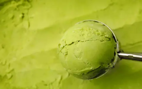 Eine Kugel cremiges Matcha-Eis wird mit einem Löffel aus einer Schüssel gehoben. Perfekt für ein erfrischendes Matcha Eis Rezept.