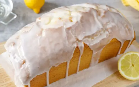 Saftiger zitronenkuchen in Kastenform, überzogen mit süßem Zuckerguss. Ein Zitronenstück liegt daneben.