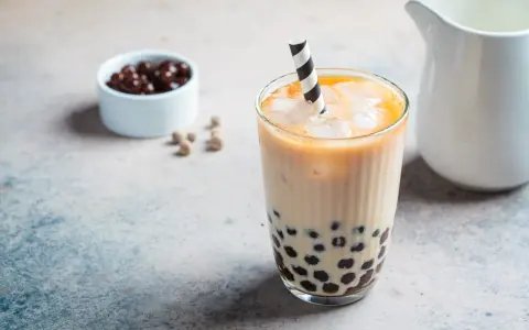Erfrischendes Bubble Eis mit Tapiokaperlen und Eiswürfeln in einem Glas, daneben eine Schale mit dunklen Perlen.