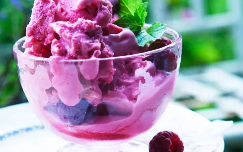Himbeereis in einer Glasschale, frisch aus der Eismaschine, garniert mit Minze und ganzen Himbeeren.