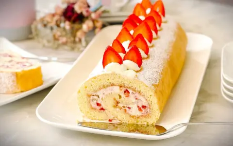 Ein köstliches Biskuitrolle Rezept mit frischen Erdbeeren und Sahne, bestäubt mit Puderzucker.