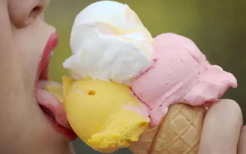 Eiscreme-Liebhaberin schleckt an einem Eis mit drei Kugeln. Die richtige guarkernmehl dosierung macht das Eis cremig.