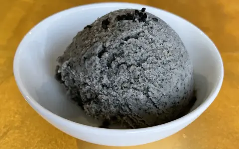 Ein Löffel cremiges Sesam Eis, garniert mit schwarzen Sesamkörnern, in einer weißen Schale.