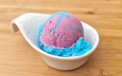 Ein Löffel eis mit kaugummi Geschmack, in rosa und blau, serviert in einer weißen Schale auf Holzuntergrund.