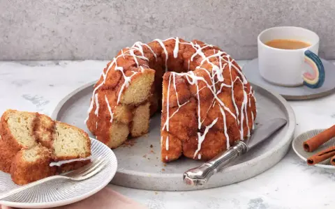 Ein köstlicher Monkey Bread mit Zimt und Zuckerguss, bereit zum Teilen. Daneben eine Tasse Kaffee und Zimtstangen.