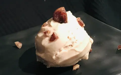Cremiges Maronen Eis, garniert mit kleinen Maronenstückchen, auf einem dunklen Teller. Ein Genuss für kalte Tage.