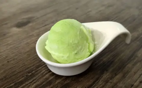 Ein Löffel cremiges Apfel-Eis in einer weißen Schale auf Holztisch.