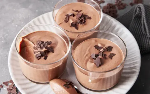 Drei Gläser mit luftiger Schokoladenmousse, garniert mit Schokostückchen. Ein Löffel zeigt die cremige Konsistenz dieses rezept mousse au chocolat ohne ei.
