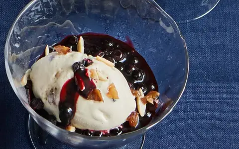 Cremiges Malaga Eis Rezept mit Blaubeersauce und Mandelsplittern in einer Glasschale.