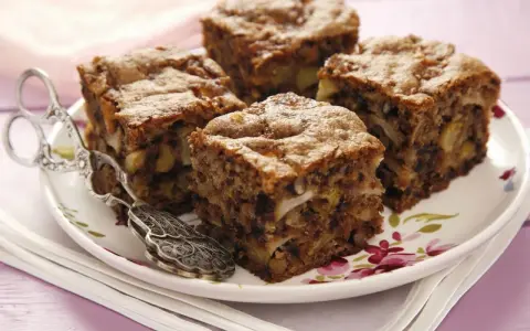 Vier Stücke saftiger Apfel Walnuss Kuchen auf einem Teller mit Blumenmuster, daneben ein antiker Tortenheber.