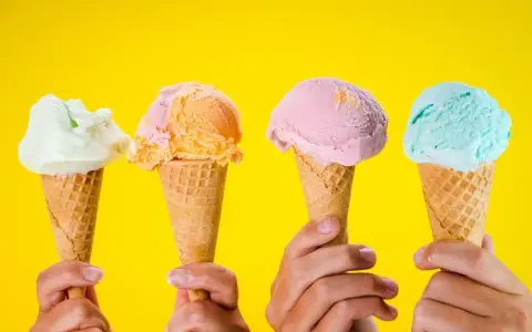 Vier Hände halten bunte Speiseeiswaffeln vor gelbem Hintergrund. Die ideale Temperatur für Speiseeis.