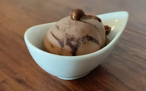 Ein Bacio Eis in einer weißen Schale, gekrönt von einer Haselnuss. Ein süßer Genuss auf Holztisch.