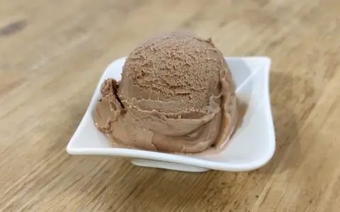 Ein Löffel cremiges Nougat Eis in einer weißen Schale auf einem Holztisch.