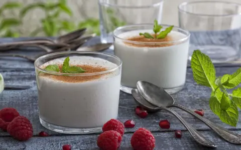 Zwei Gläser cremiger Leche Merengada, garniert mit Minze und Zimt, umgeben von Himbeeren und Granatapfelkernen.