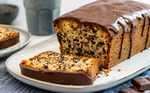Ein saftiger Stracciatella Kuchen mit Schokoladenglasur, ein Stück davon auf einem Teller.