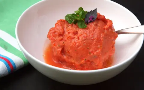 Ein erfrischendes Tomaten-Eis, garniert mit Basilikum, in einer weißen Schüssel.