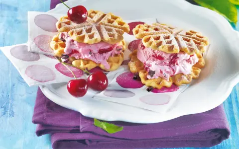 Zwei herzförmige Waffeln gefüllt mit Kirscheis und Schokostückchen, garniert mit frischen Kirschen. Ein süßer Genuss!