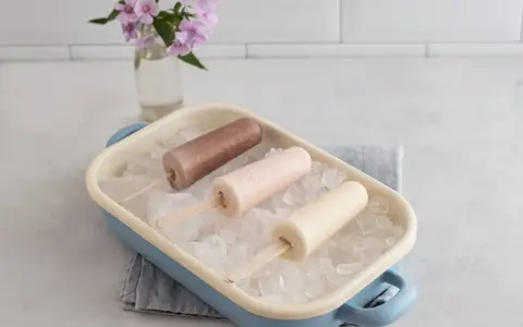 Drei cremige Mini Milk Eis am Stiel, wie aus den 90ern, in einer blauen Schale auf Eiswürfeln.