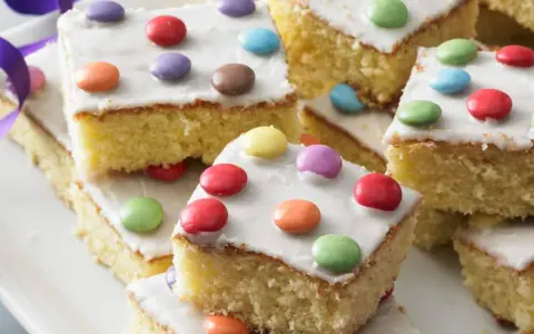 Bunter Fantakuchen-Rezept: saftige Kuchenstücke mit weißer Glasur und bunten Smarties. Perfekt für Kindergeburtstage!