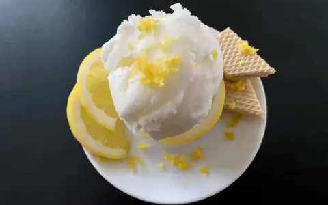 Erfrischendes zitroneneis wie beim Italiener, garniert mit Zitronenschale, Zitronenscheiben und Waffeln auf einem weißen Teller.