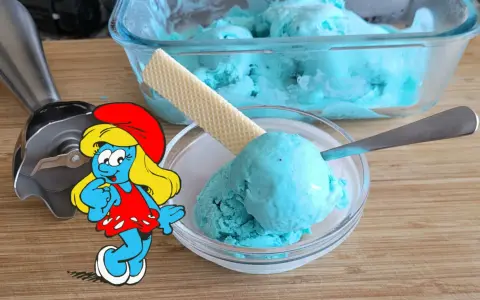 Schlumpfine genießt engelblaues Eis. Ein Handmixer und ein Waffelblatt liegen daneben.
