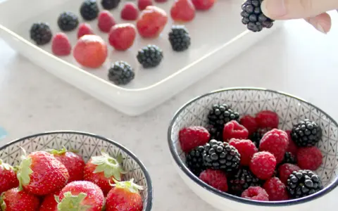 Frische Beeren, darunter Erdbeeren, Himbeeren und Brombeeren, werden für die Lagerung vorbereitet. Man kann Erdbeeren einfrieren, um sie später zu genießen.