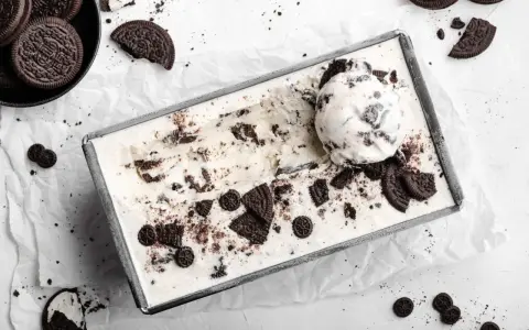 Cremiges Oreo Eis in einer Metallform, garniert mit ganzen und zerbrochenen Keksen. Ein Löffel Eis liegt obenauf.