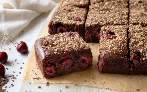 Saftiger kirschkuchen mit frischen kirschen, bestreut mit Nüssen. Daneben liegen frische Kirschen und Schokostückchen.