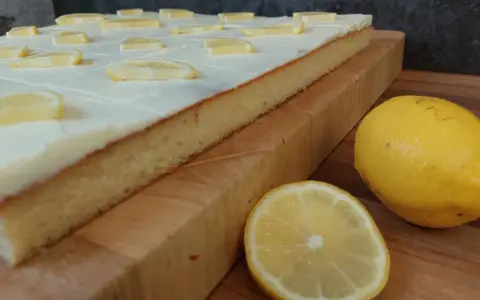 Ein saftiger sizilianischer Zitronenkuchen, bedeckt mit weißer Glasur und Zitronenscheiben, daneben frische Zitronen.