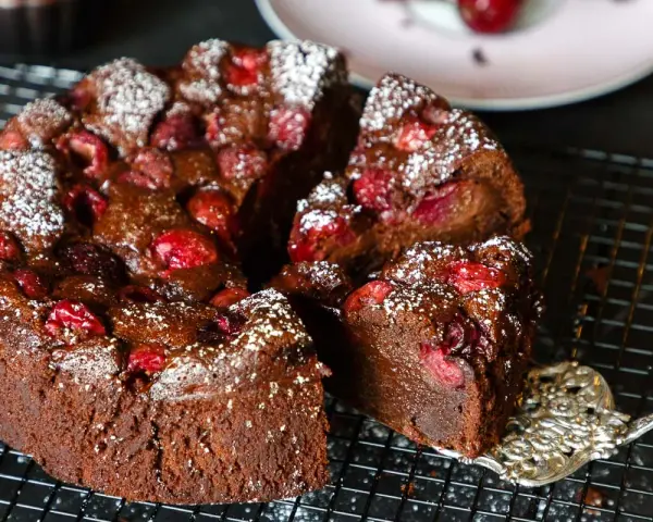 Ein saftiger schoko kirsch kuchen, bestäubt mit Puderzucker, wird auf einem Gitter präsentiert. Eine Gabel hebt ein Stück ab.