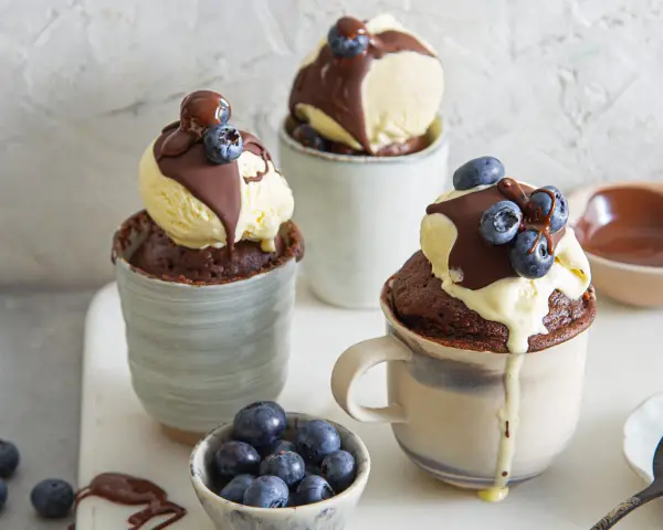 Schokoladiger Tassenkuchen mit Vanilleeis, Schokosauce und Blaubeeren. Ein schnelles Tassenkuchen Rezept für süße Momente.