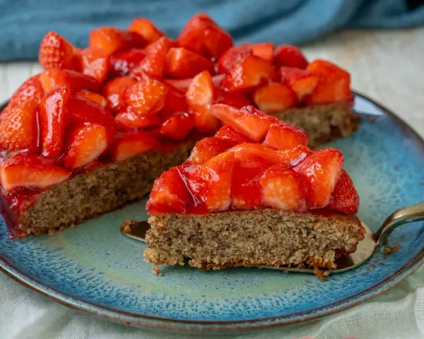 Ein saftiger glutenfreier Erdbeerkuchen mit frischen Erdbeeren und glänzender Tortenglasur auf einem blauen Teller.