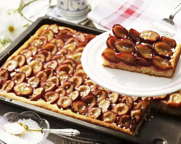 Ein saftiger Zwetschgenkuchen vom Blech, mit süßen Früchten und Zucker bestreut, wartet darauf, genossen zu werden.