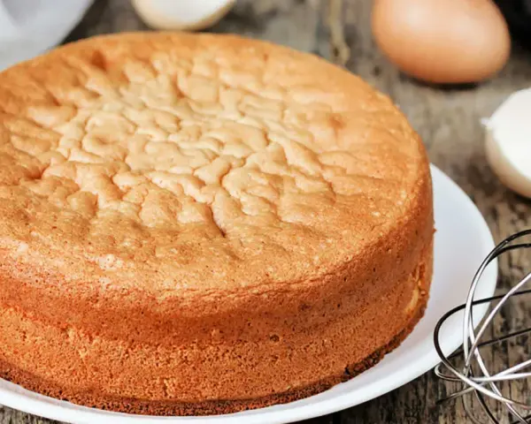 Perfekter Biskuitboden: Ein goldbrauner Kuchen, bereit für Ihr nächstes biskuitboden rezept. Eier und Schneebesen deuten auf die Zubereitung hin.