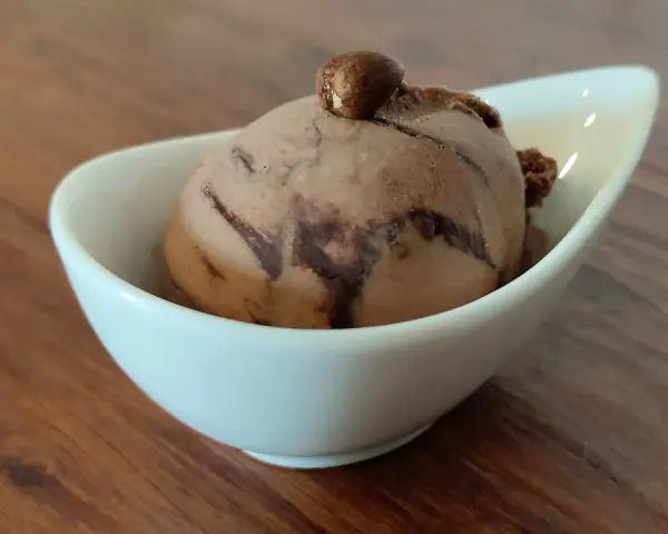 Ein Bacio Eis in einer weißen Schale, gekrönt von einer Haselnuss. Ein süßer Genuss auf Holztisch.