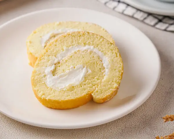 Zwei Scheiben einer leichten Biskuitrolle mit cremiger Füllung, perfekt für ein Zitronenrolle Rezept.
