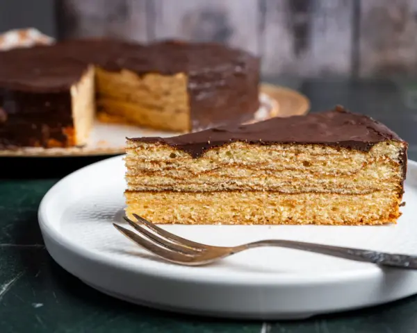Ein Stück Schokoladen-Baumkuchen mit vielen Schichten liegt auf einem Teller. Das Baumkuchen Rezept ist ein Klassiker.
