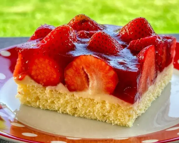 Ein saftiges Stück Erdbeerkuchen vom Blech, belegt mit frischen Erdbeeren und Tortenguss.