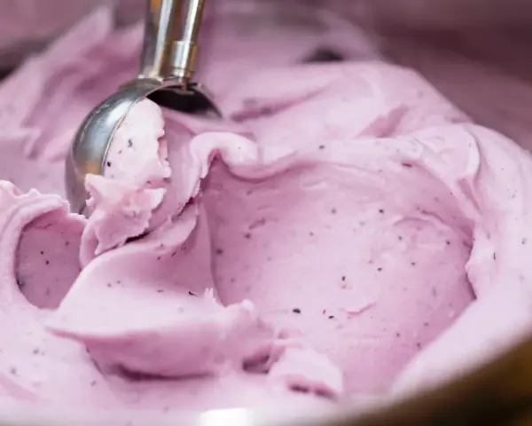Ein Löffel nimmt eine Portion cremiges, kalorienarmes Eis mit Beerenstücken auf.
