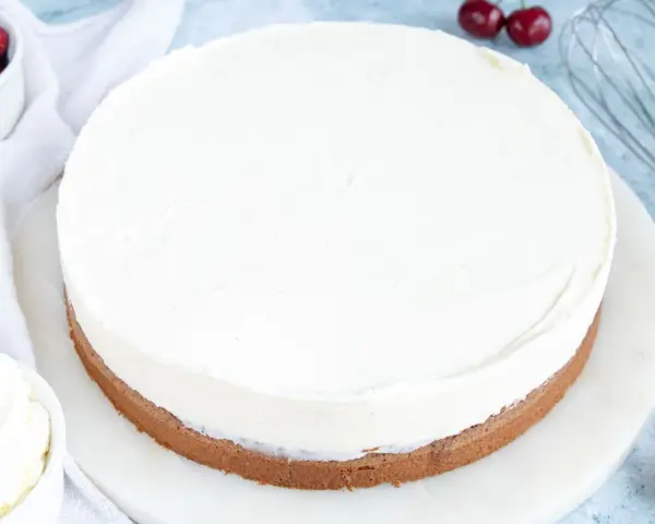 Ein köstlicher Kuchen mit Mascarpone-Creme, garniert mit frischen Kirschen und einem Schneebesen daneben.