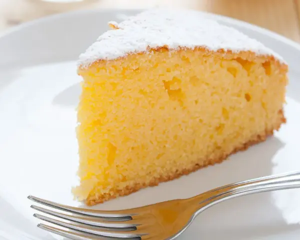 Ein saftiges Stück vanille kuchen, bestäubt mit Puderzucker, wartet auf einer weißen Platte mit einer Gabel.
