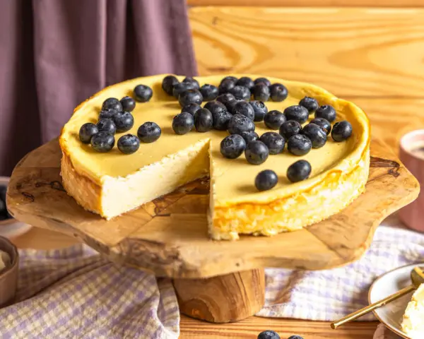 Ein köstlicher Skyr Kuchen, üppig belegt mit frischen Blaubeeren, wartet auf seine Genießer. Daneben eine Tasse Kaffee.