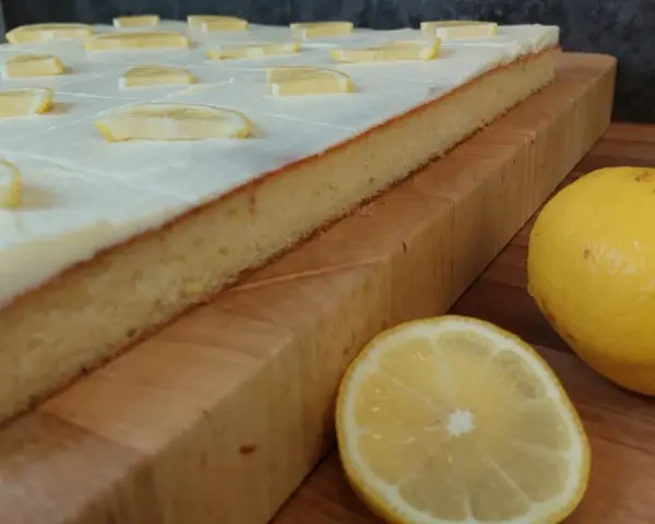 Ein saftiger sizilianischer Zitronenkuchen, bedeckt mit weißer Glasur und Zitronenscheiben, daneben frische Zitronen.