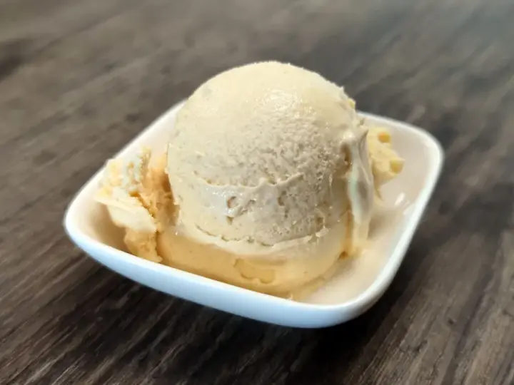 Cremiges Dulce de Leche Eis in einer weißen Schale auf Holzhintergrund.