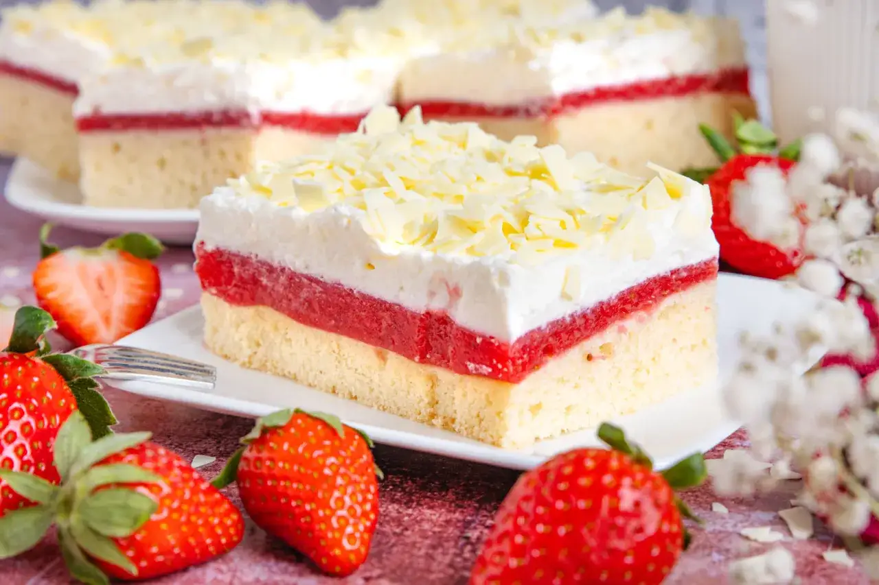 Ein saftiger Frau Holle Kuchen mit Erdbeerfüllung und weißer Schokoladenspäne, garniert mit frischen Erdbeeren.