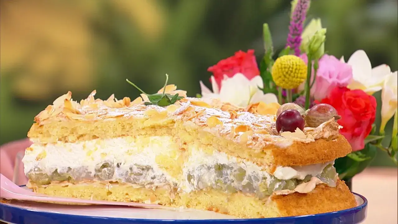 Ein saftiger Stachelbeer Baiser Kuchen mit Mandelsplittern und frischen Beeren, dekoriert mit bunten Blumen.