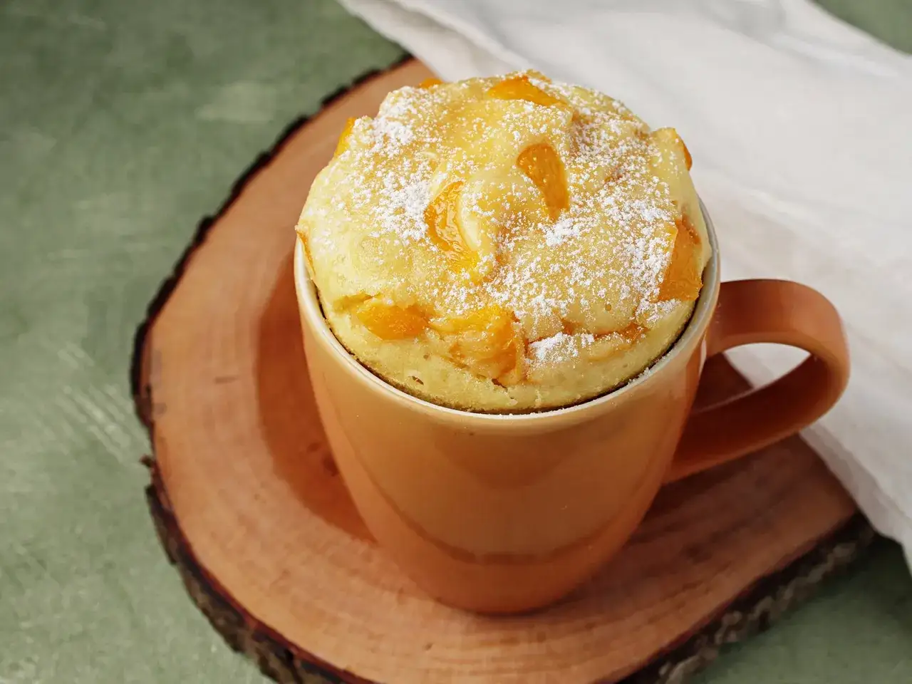 Ein leckerer Tassenkuchen mit Pfirsichstücken, bestäubt mit Puderzucker. Ein schnelles und einfaches Tassenkuchen Rezept für zwischendurch.