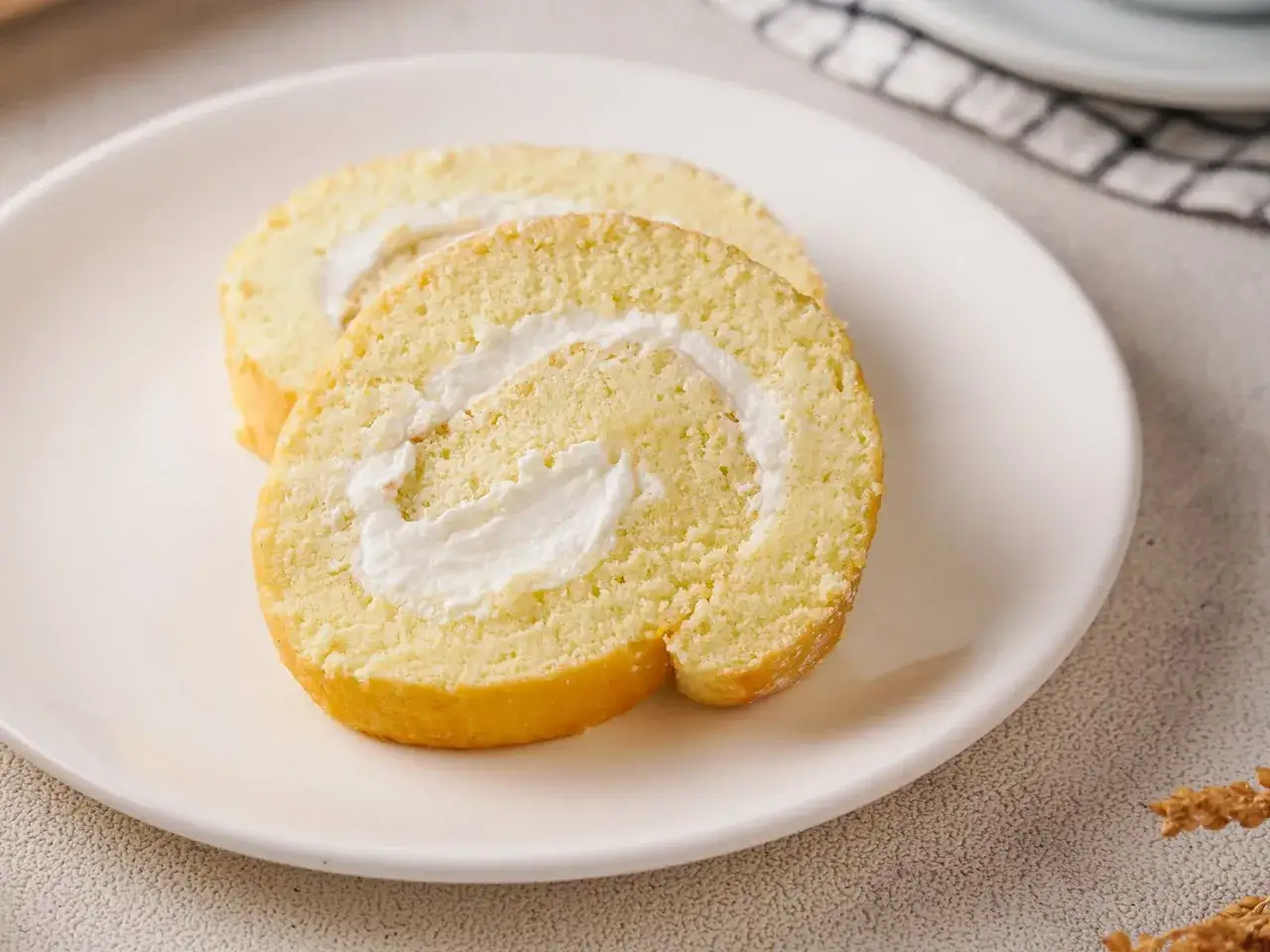 Zwei Scheiben einer leichten Biskuitrolle mit cremiger Füllung, perfekt für ein Zitronenrolle Rezept.