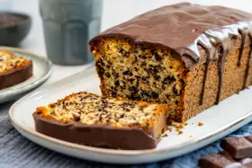 Ein saftiger Stracciatella Kuchen mit Schokoladenglasur, ein Stück davon auf einem Teller.